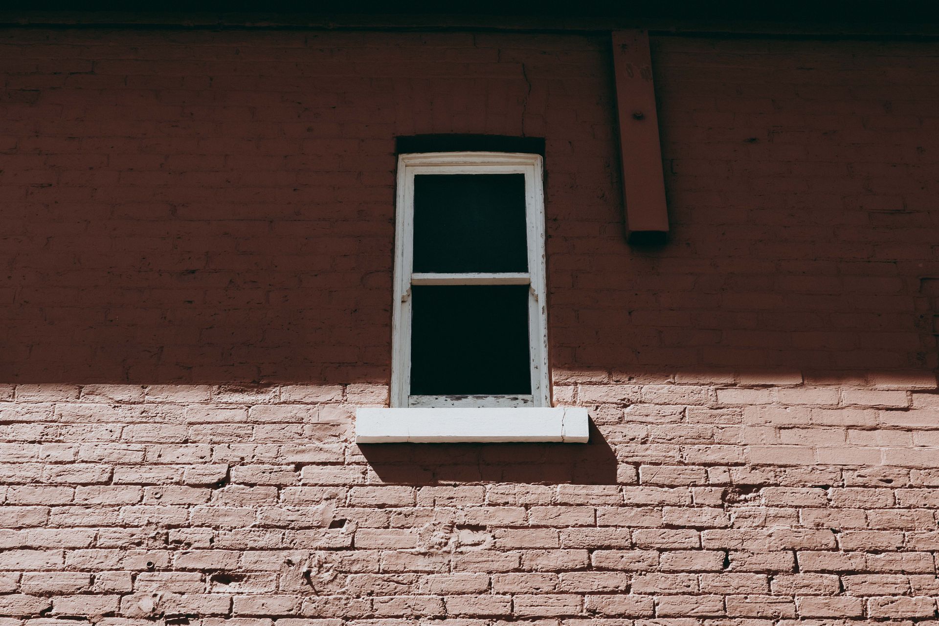 Small white-framed window on a red brick wall with a narrow sill