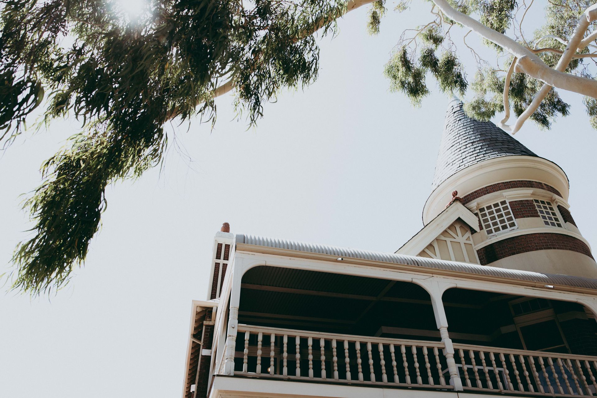 Low-angle view of a white building with a pointed tower framed by tree branches against the sky