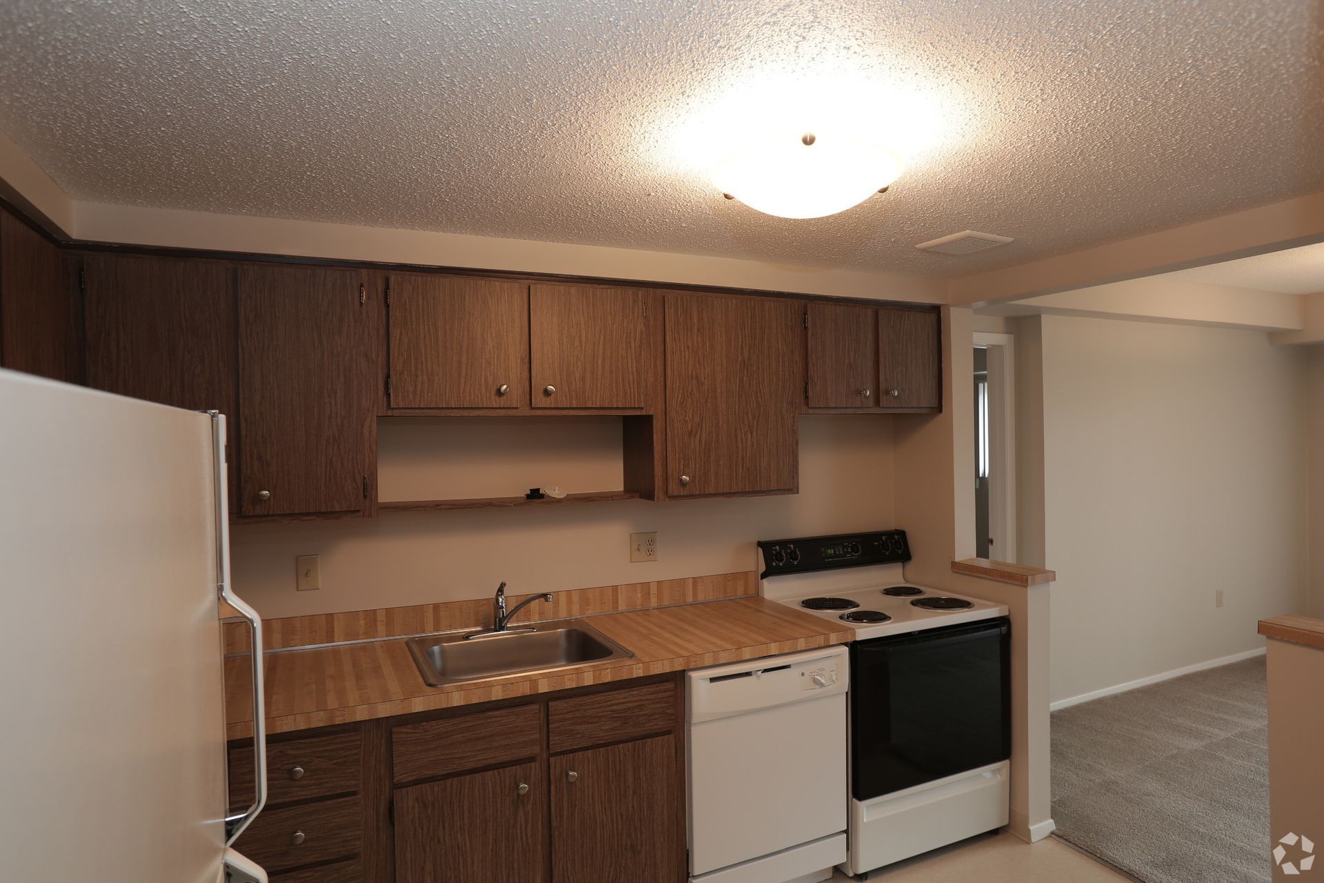 An empty kitchen with wooden cabinets and a white refrigerator