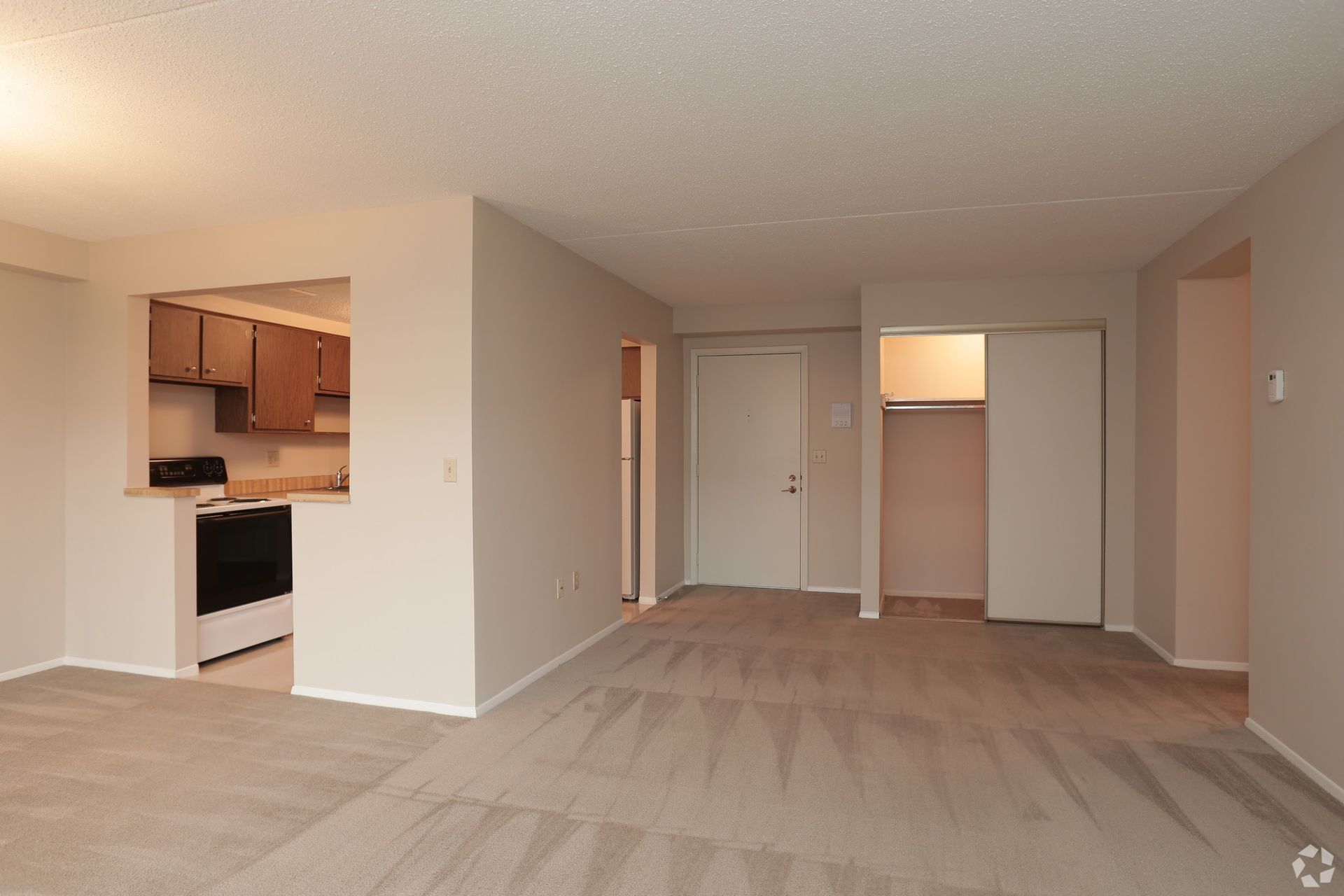 An empty living room with a kitchen in the background