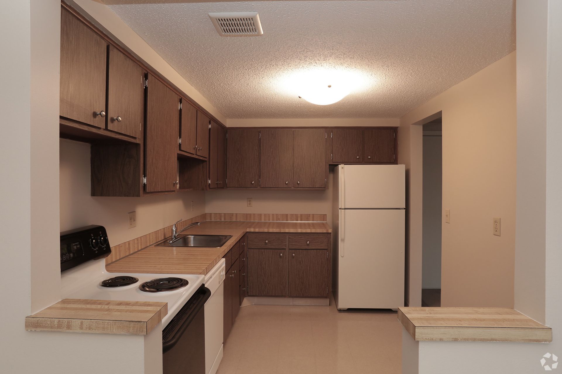 An empty kitchen with brown cabinets and a white refrigerator