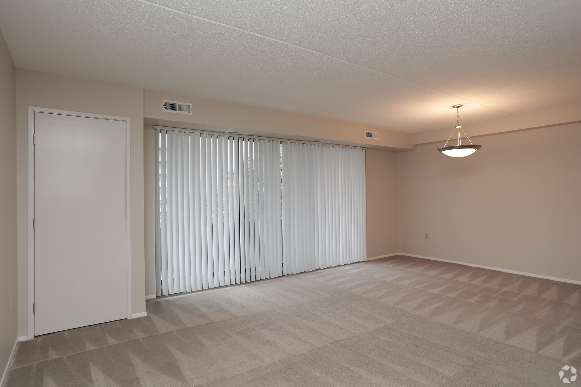 An empty living room with sliding glass doors and blinds