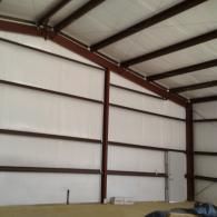 Interior view of a warehouse with metal walls and a gabled roof, featuring red structural beams and a single entry door.