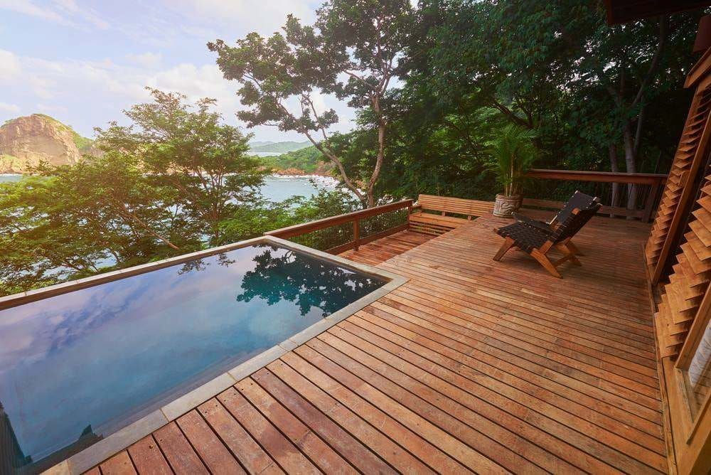 Wooden Deck With Infinity Pool, Lounge Chairs, and Ocean View at Sunset — Professional Pool Builder in Wagga Wagga, NSW