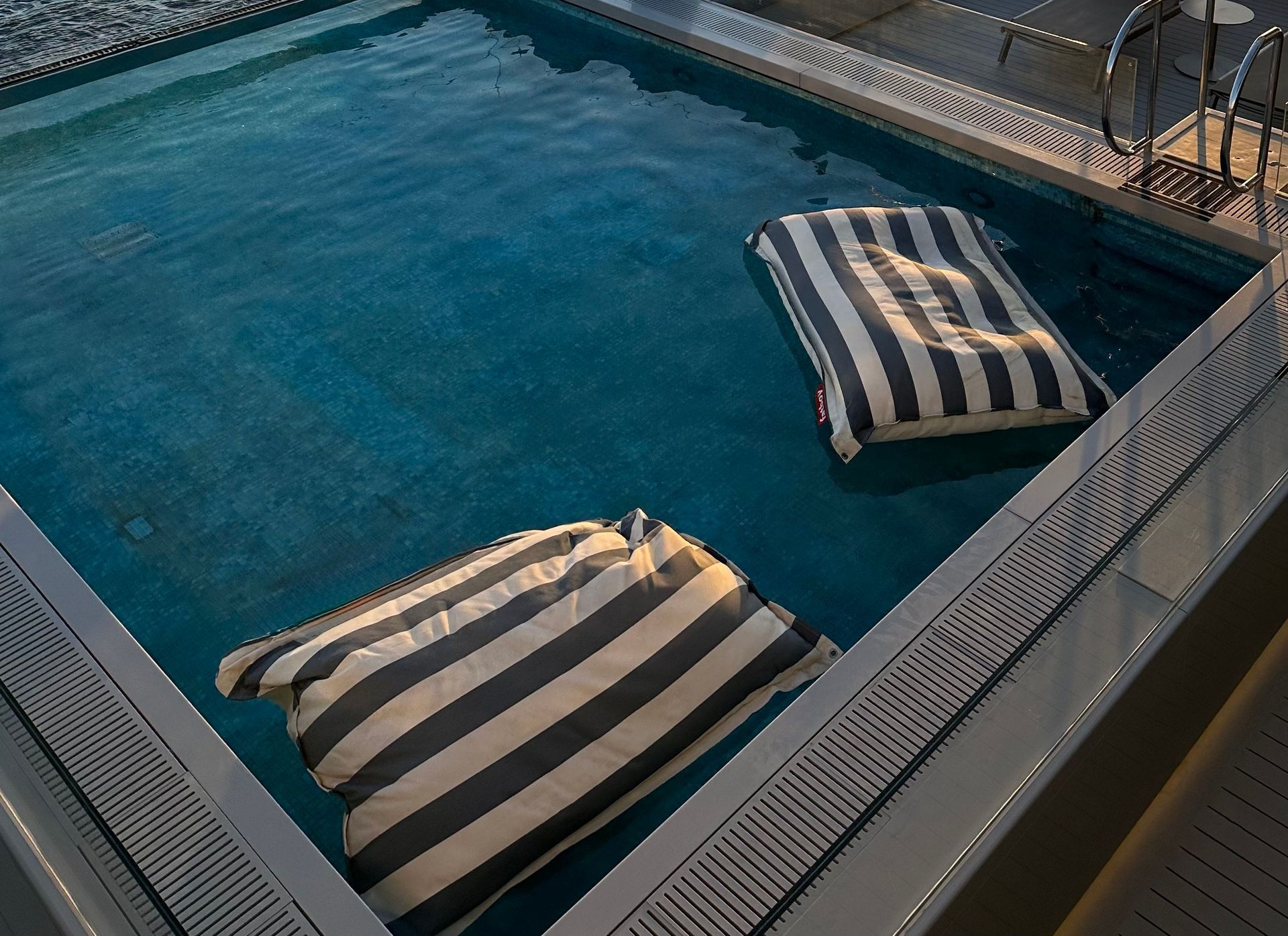 Wooden Deck With Infinity Pool, Lounge Chairs, and Ocean View at Sunset — Professional Pool Builder in Wagga Wagga, NSW