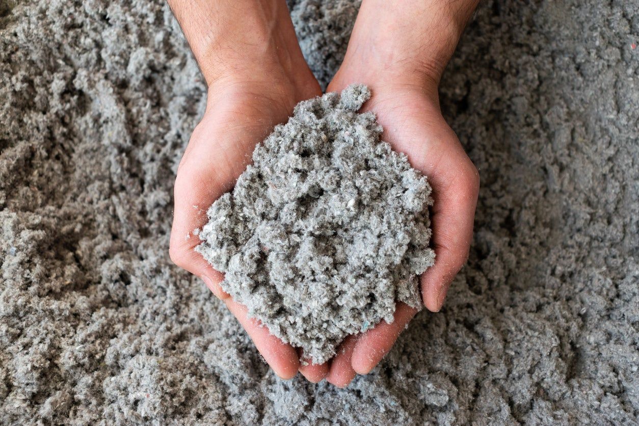 A person is holding a pile of cellulose insulation in their hands.