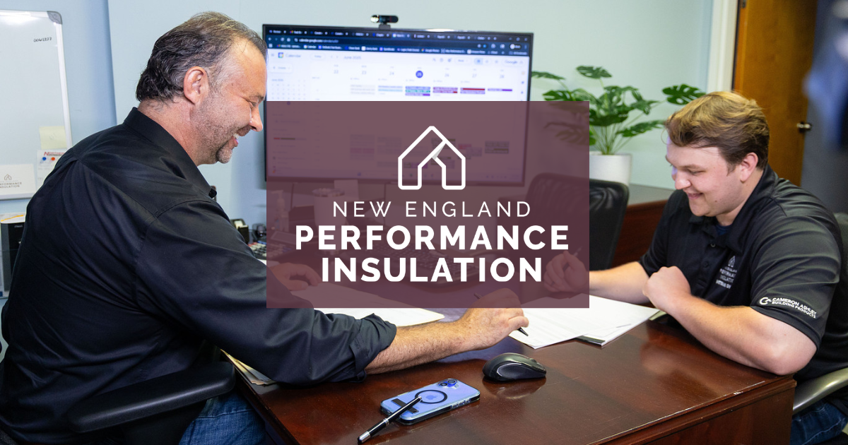 Two people at a desk reviewing a laptop in an office, with a “New England Performance Insulation” sign on screen