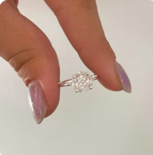Mano sosteniendo un pequeño anillo de plata con un grupo de piedras transparentes sobre un fondo claro.