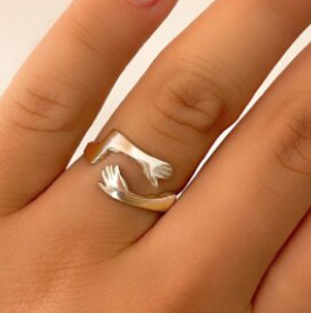 Primer plano de una mano que lleva un anillo de plata con dos manos formando un corazón.