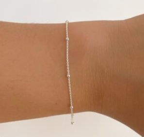 Pulsera de cuentas de plata en una muñeca sobre un fondo claro.