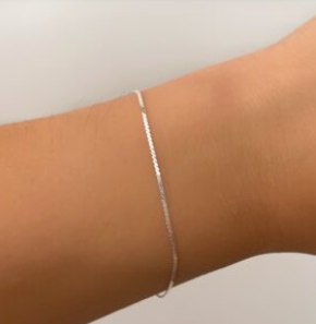 Primer plano de una muñeca con una fina pulsera de plata sobre un fondo claro.