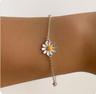 Pulsera blanca con margaritas y centro amarillo en la muñeca sobre un fondo beige.