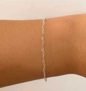 Pulsera de cadena plateada en una muñeca sobre un fondo neutro.