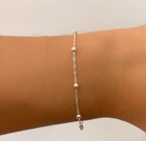 Pulsera de cuentas de plata en una muñeca sobre un fondo liso.