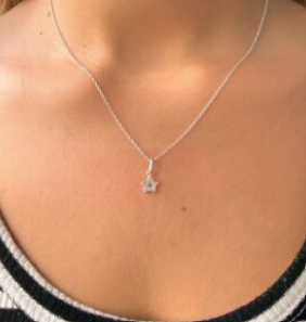 Primer plano de un collar de plata con un pequeño colgante en el cuello y el pecho de una persona.
