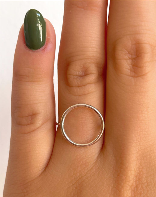 Primer plano de los dedos con esmalte de uñas verde oliva y un fino anillo plateado en uno de ellos.