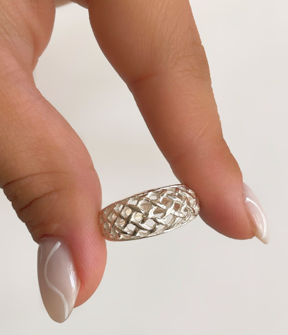 Mano sosteniendo un pequeño anillo plateado texturizado entre el pulgar y el dedo índice.