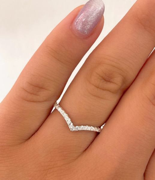 Mano que lleva un anillo plateado con forma de chevrón y piedras brillantes en un dedo.