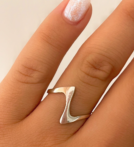 Primer plano de una mano con un anillo geométrico plateado y una manicura rosa pálido.