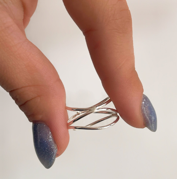 Mano sosteniendo una pinza para el cabello plateada y retorcida con uñas azules brillantes.