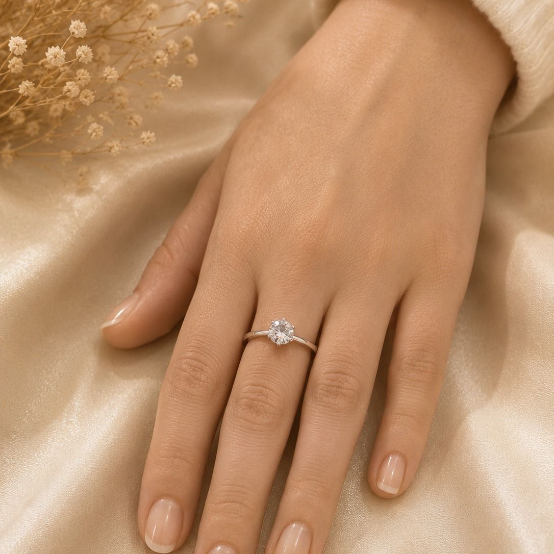 Mano con un anillo de plata sobre un fondo de tela satinada beige.