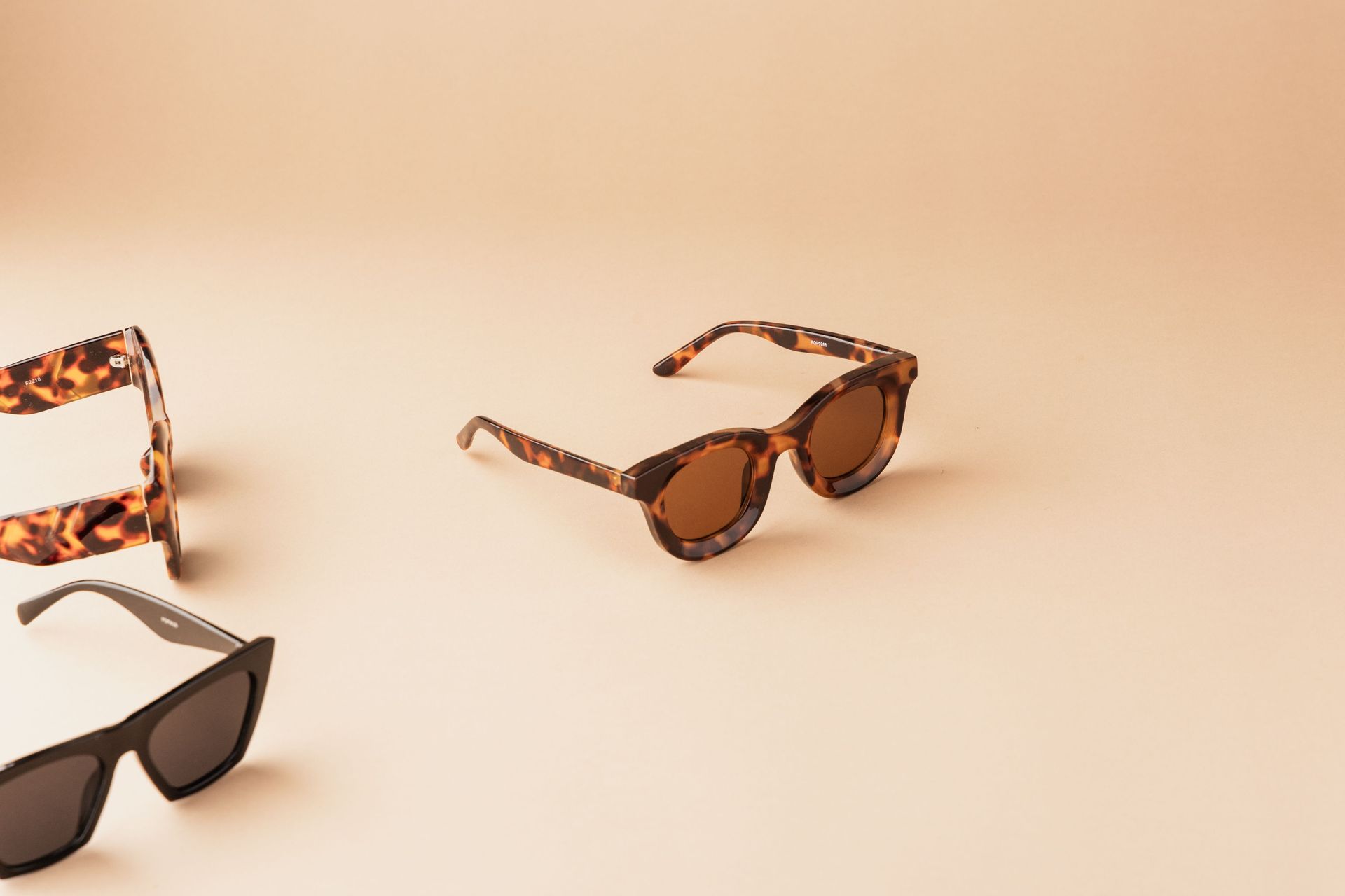 Tres pares de gafas de sol sobre una superficie beige, incluyendo monturas marrones y de carey.