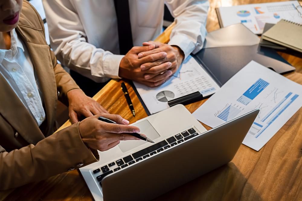 A Man and A Woman Are Sitting at A Table Looking at A Laptop Computer — Sunshine Coast Financial Advisers in Caloundra, QLD