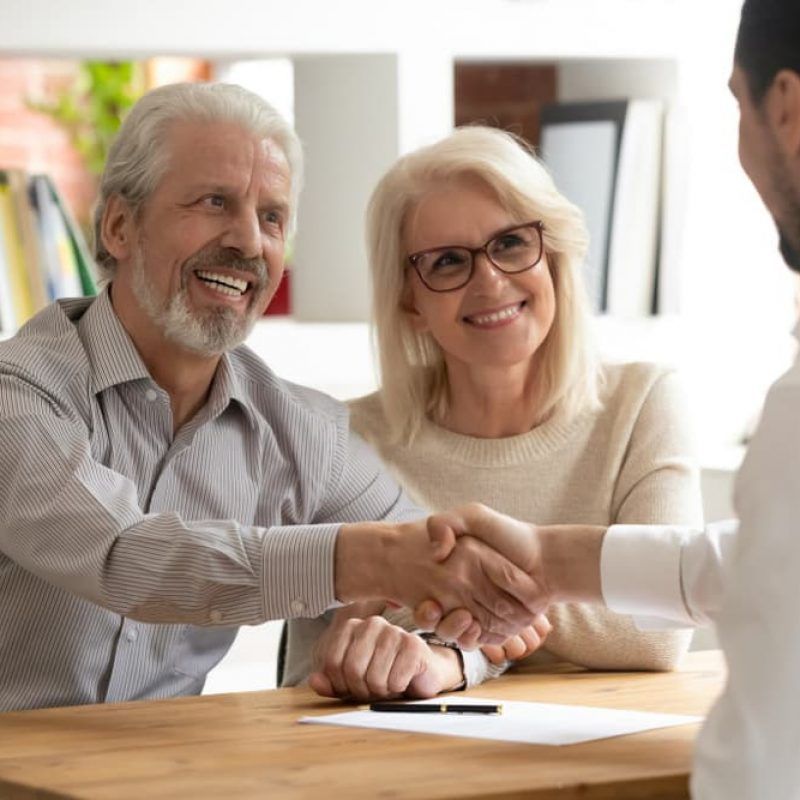 A Man and Woman Are Shaking Hands While Sitting at A Table — Sunshine Coast Financial Advisers in Maroochydore, QLD