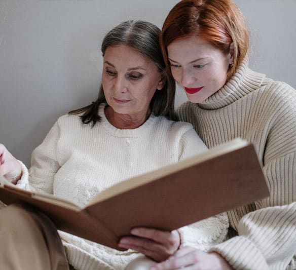 Two Women Are Sitting Next to Each Other Reading a Book — Sunshine Coast Financial Advisers in Maroochydore, QLD
