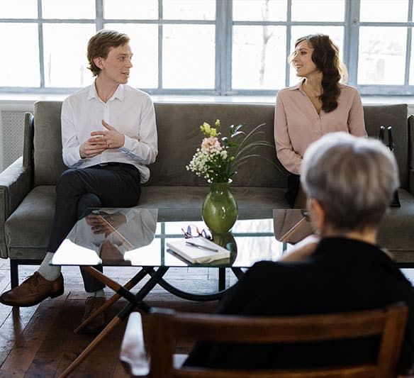 A Man and A Woman Are Sitting on A Couch Talking to Each Other — Sunshine Coast Financial Advisers in Maroochydore, QLD