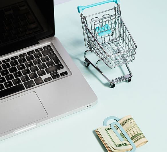 A Stack of Money Next to A Shopping Cart and A Laptop — Sunshine Coast Financial Advisers in Maroochydore, QLD