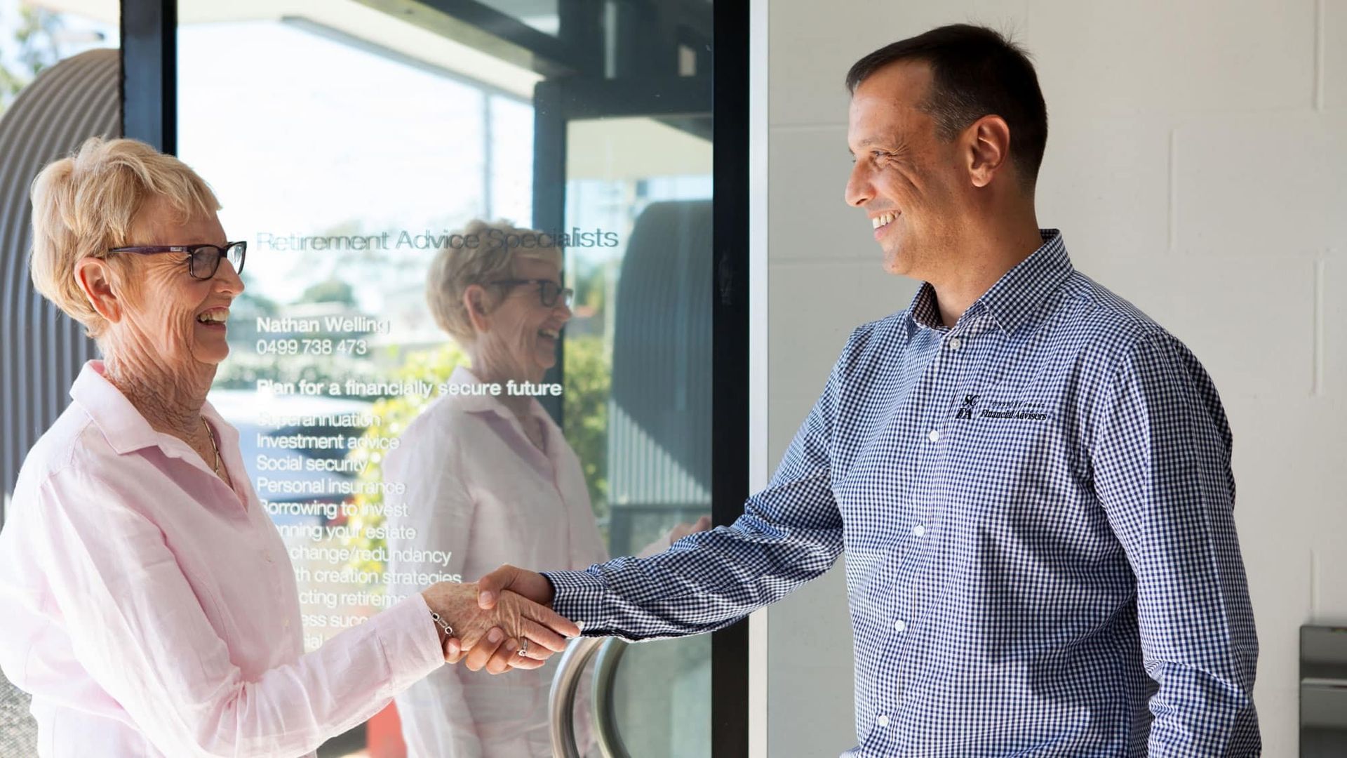 A Man and A Woman Are Shaking Hands in Front of A Window — Sunshine Coast Financial Advisers in Maroochydore, QLD