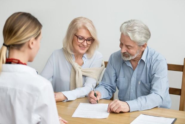 An Elderly Couple Is Signing a Document While Sitting at A Table with A Doctor