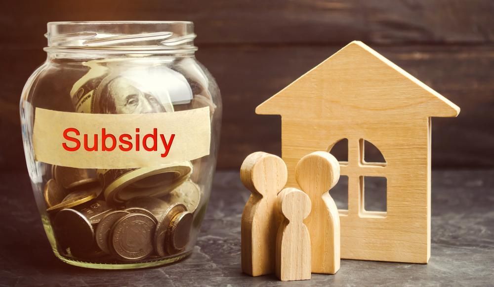 A Jar Filled with Coins Next to A Wooden House and Two Wooden Figures