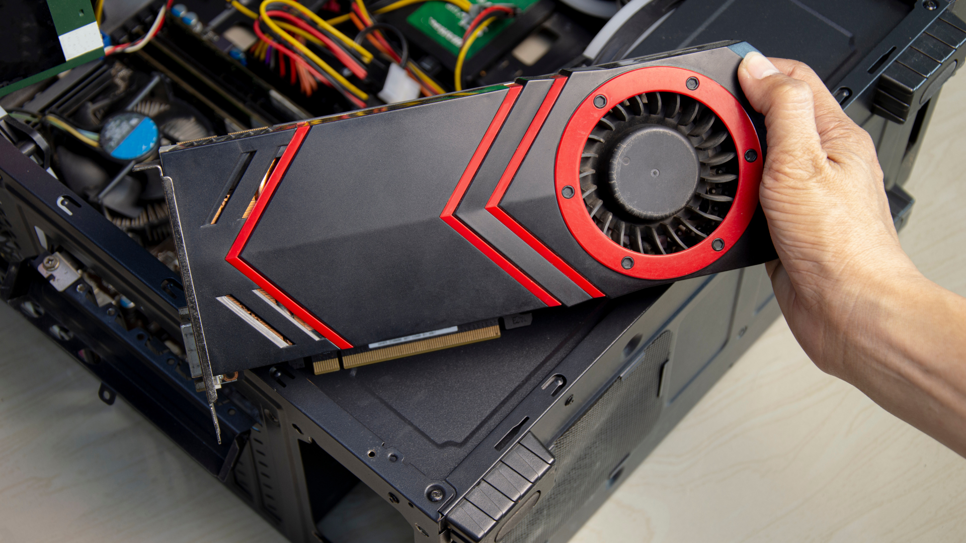Hand holding a black and red graphics card over a computer case, about to install it.