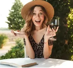 A woman in a hat is sitting at a table holding a glass of wine.