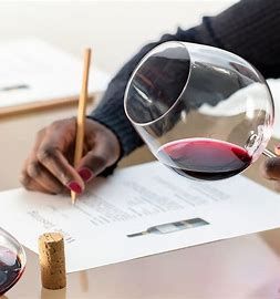 A person is writing on a piece of paper next to a glass of wine.
