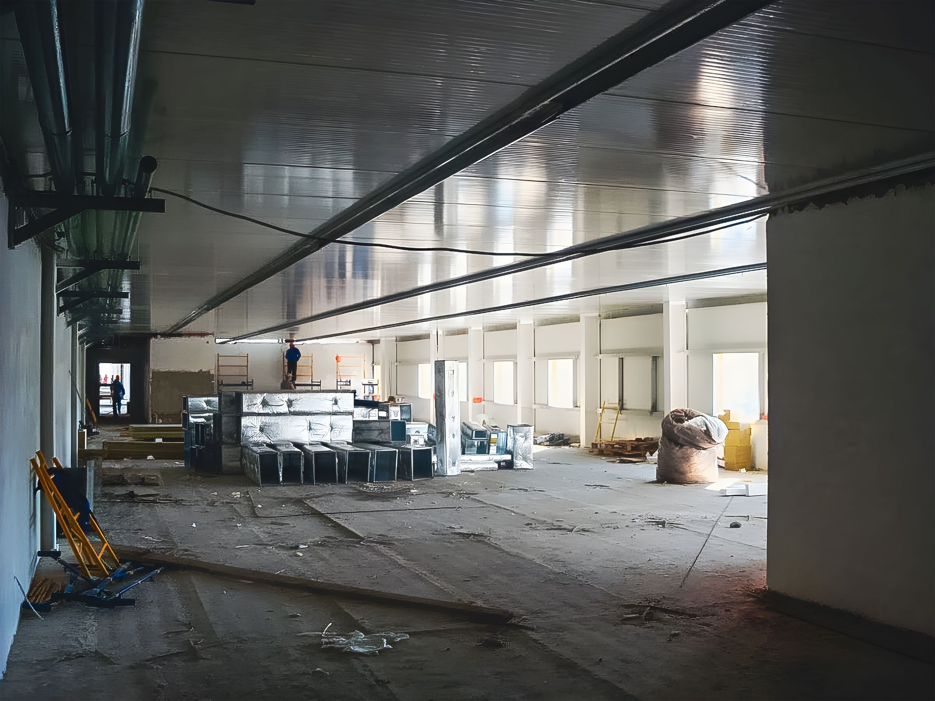 Empty industrial hallway under construction with debris, equipment, and daylight from windows on the right. Empty industrial hallway under construction with debris, equipment, and daylight from windows on the right.
