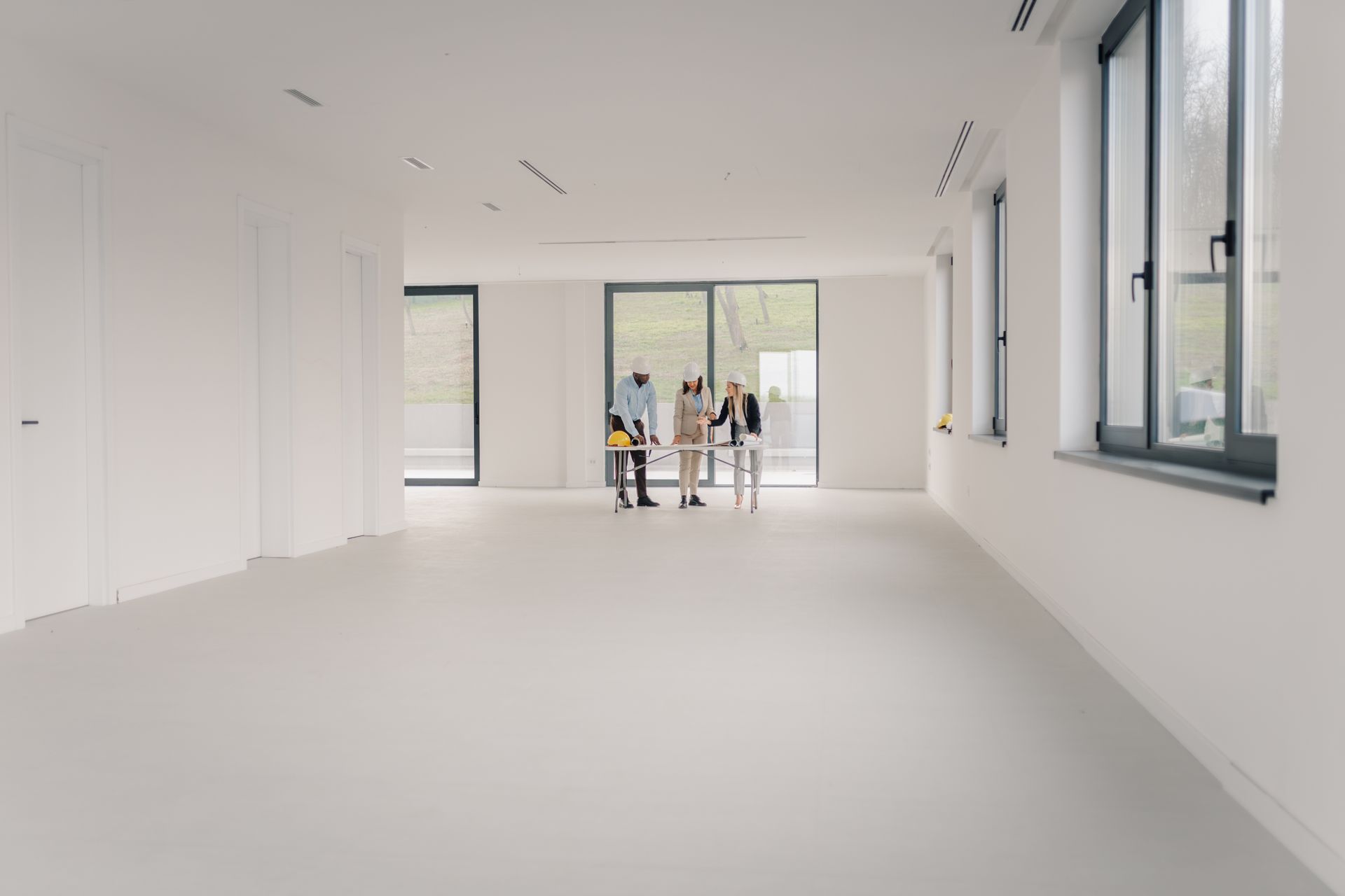 Bright empty white room with large windows and a few people near the far glass doors Bright empty white room with large windows and a few people near the far glass doors
