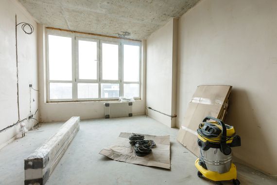 Renovation room with bare walls, large window, construction materials, and a shop vacuum on the floor Renovation room with bare walls, large window, construction materials, and a shop vacuum on the floor
