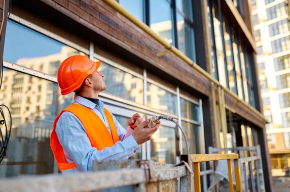 Construction worker in orange hard hat and vest inspecting a building site with a tablet Construction worker in orange hard hat and vest inspecting a building site with a tablet