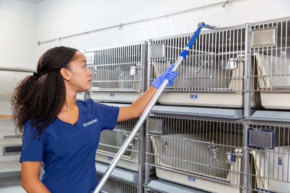 Laboratory animal science professional using High Duster to clean top of cage rack