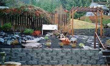 A backyard with a stone wall , stairs , and a pergola.