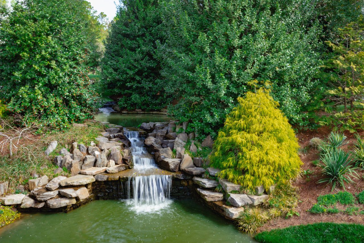 A small waterfall is surrounded by trees and rocks in a park.