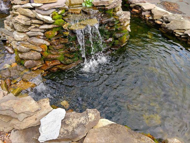There is a waterfall in the middle of a pond surrounded by rocks.