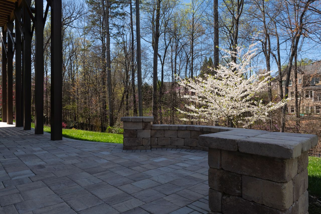 A patio with a stone wall and a tree in the background.