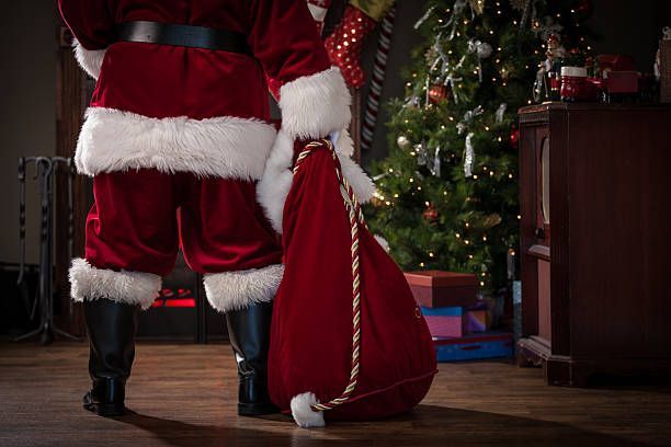 Two santa clauses are standing next to each other in front of a christmas tree.