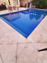 A rectangular blue swimming pool set in a backyard patio area with outdoor seating and house exterior in the background.