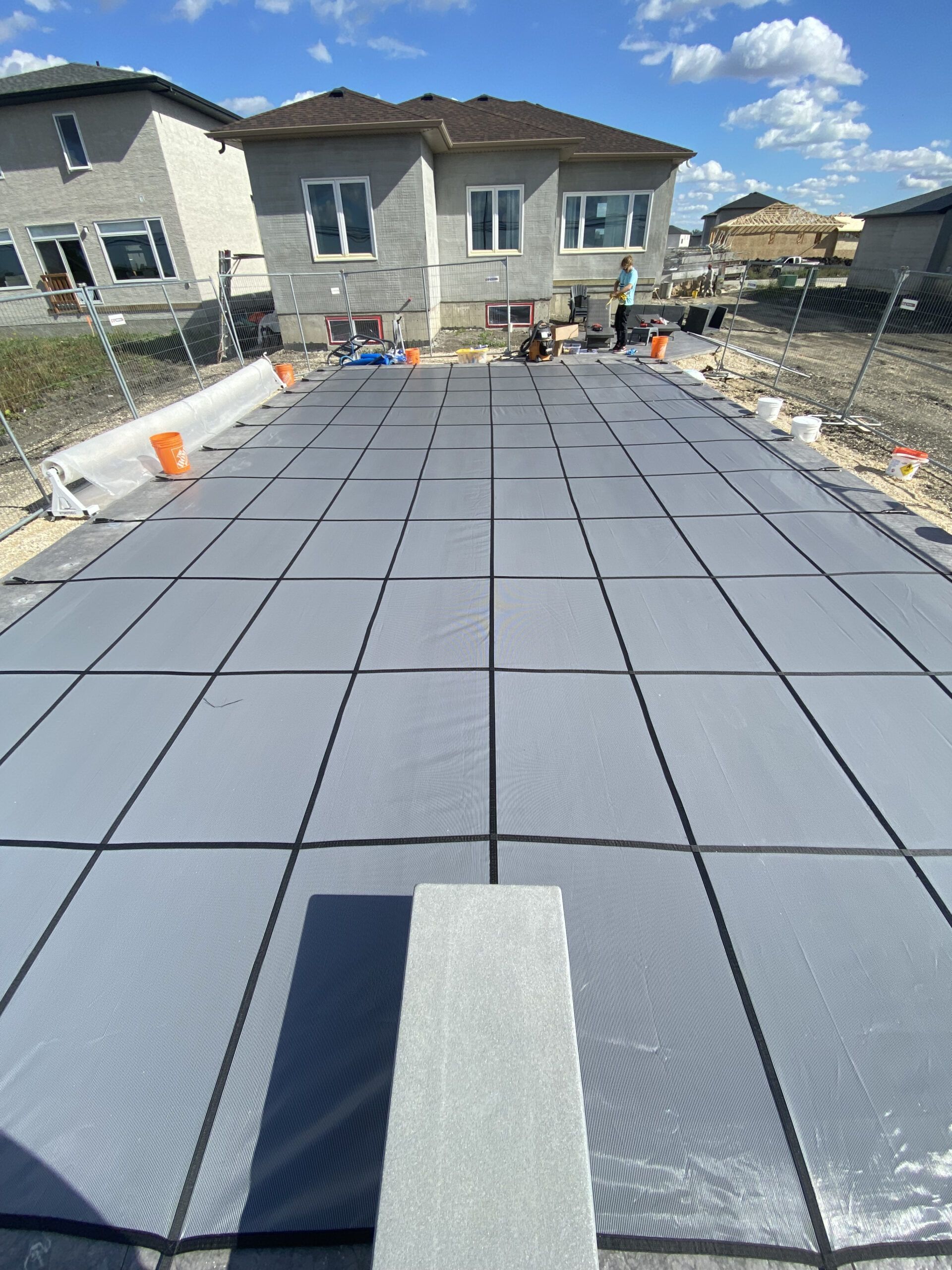 A rectangular mesh pool cover laid out on a construction site with houses in the background.