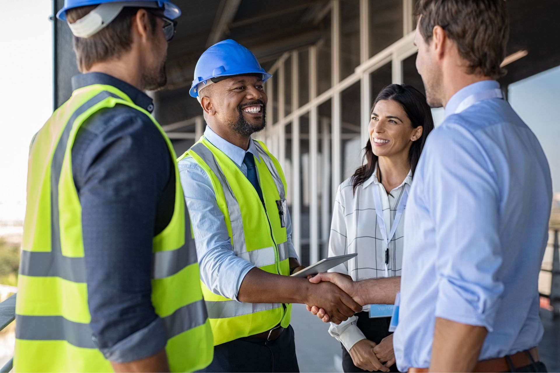 A group of professionals in high-visibility vests and business casual attire shake hands on a construction site.